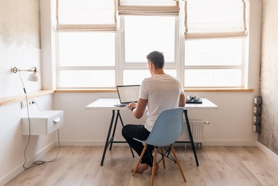Modern-young-handsome-man-in-casual-outfit-sitting-at-table-working-on-laptop-freelancer-at-home